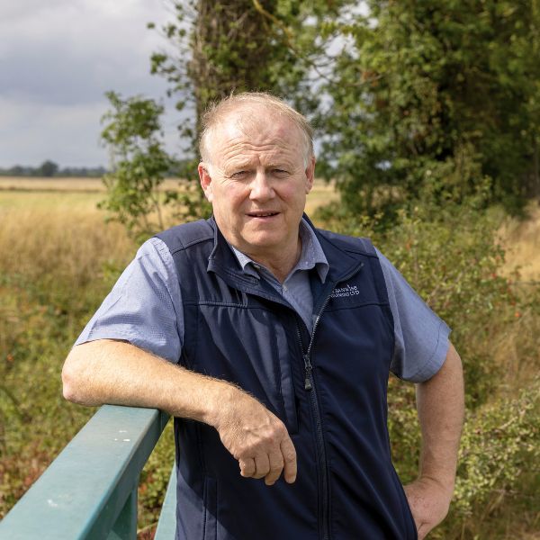 A man (Phil Jarvis) wearing a blue shirt and gilet leaning against a gate in a field